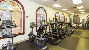 A gym with multiple treadmills and exercise bikes, large windows with arched tops, and a ceiling with fluorescent lighting.