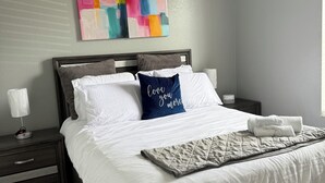 A neatly made bed with white and blue pillows, a quilt, and a bedside lamp on a dark wooden nightstand.