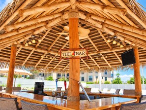 Un bar de style tiki, avec un toit de chaume, des piliers en bois et un comptoir avec des tabourets.
