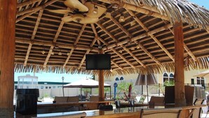 An outdoor bar area with a thatched roof, wicker furniture, and a flat-screen TV.