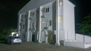 A multi-story building with a flat roof and a driveway leading to a parked car.