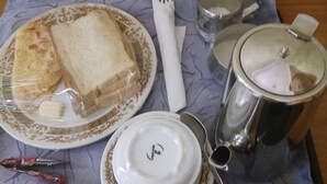 A table with a plate of sandwiches, a cup, a fork, a spoon, and a thermos.