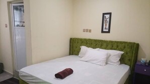 A neatly made bed with a green headboard, a white bedspread, and a rolled-up towel on the footboard.