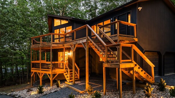 A modern wooden cabin with multiple decks and a staircase leading to the main entrance.