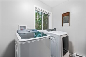 A laundry room with two white washers and dryers, a window, and a wall-mounted sign.
