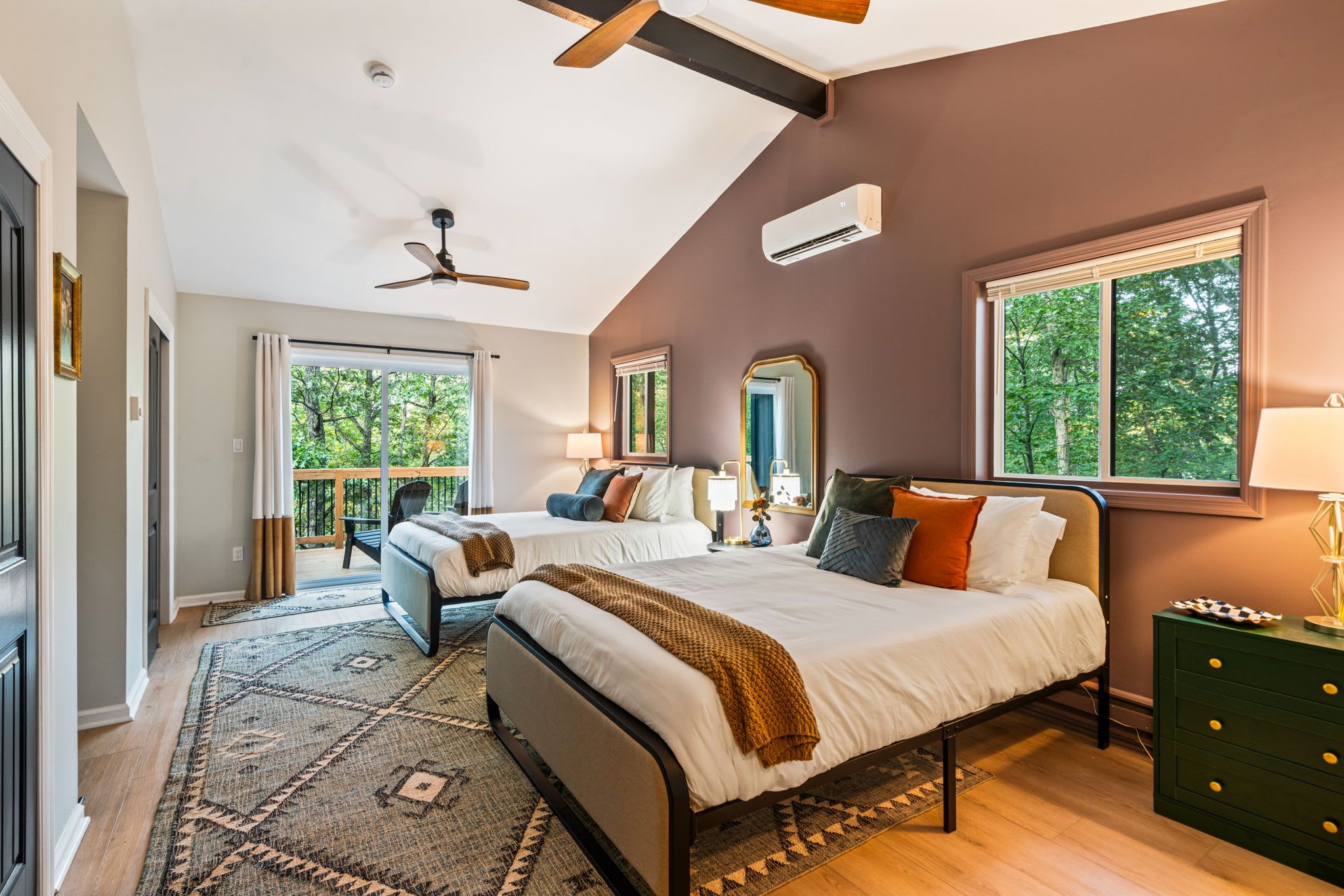 A bedroom with two beds, a ceiling fan, a large window, and a view of trees.