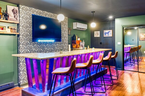 Un espace bar équipé d'un téléviseur, de tabourets de bar et d'un mur décoré de motifs.