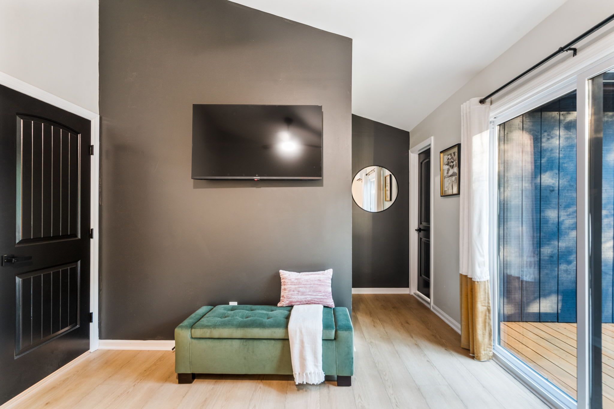 Un salon moderne avec un canapé vert, un téléviseur à écran plat fixé au mur et une grande fenêtre donnant sur le ciel.