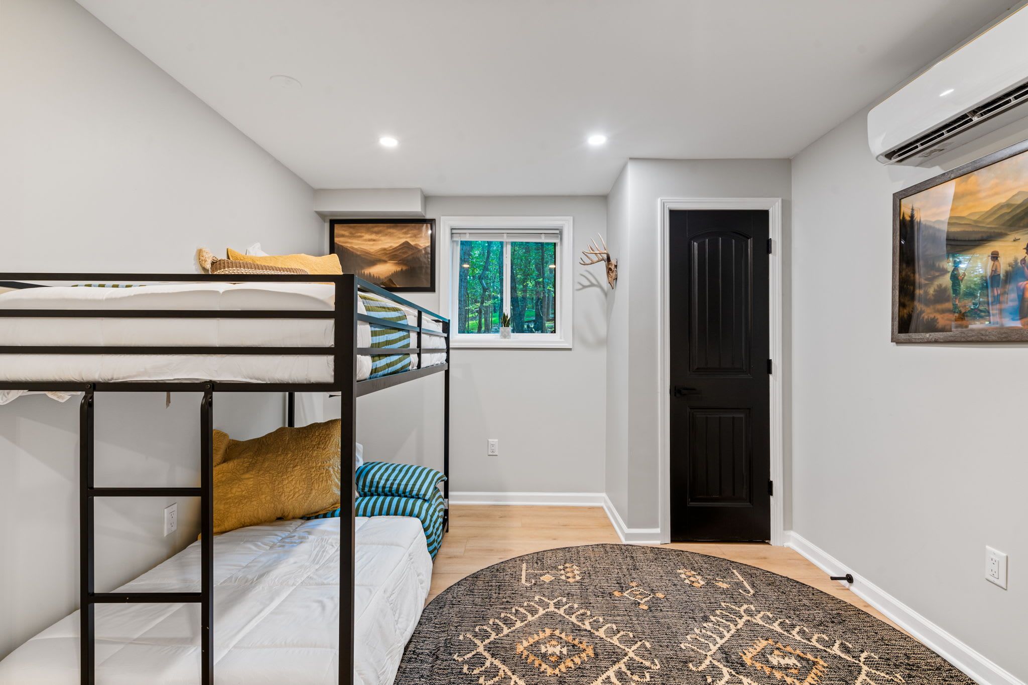 A room with a bunk bed, a window with a forest view, a black door, and a patterned rug.