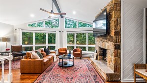 A spacious living room with a stone fireplace, large windows, and a cozy seating area.