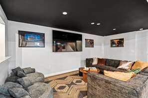 Una sala de estar moderna con techo oscuro, un sofá gris grande, una mesa de centro redonda y una alfombra estampada.