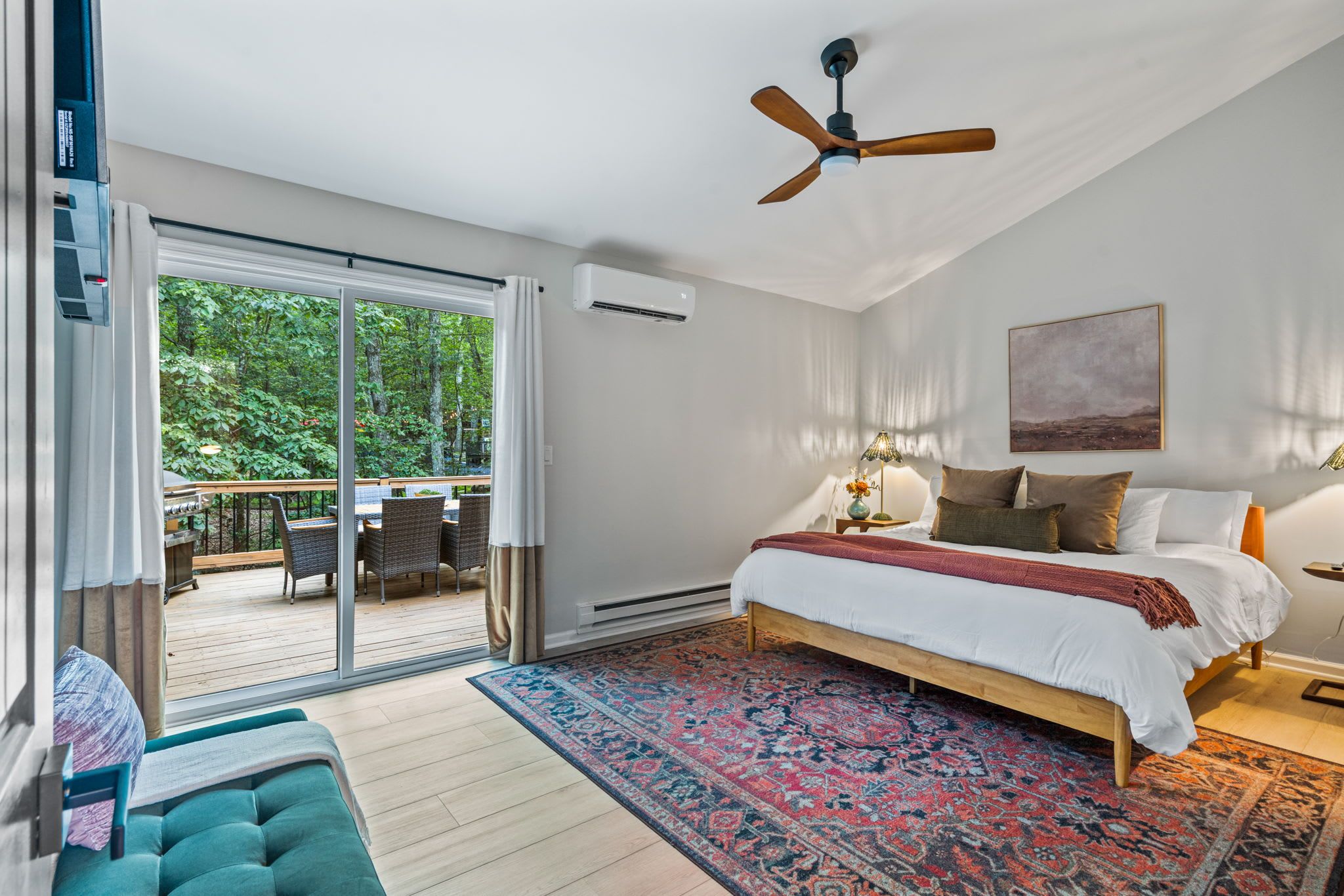 A bedroom with a large bed, a ceiling fan, a view of a balcony, and a large window.