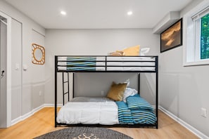 Habitación con literas, una escalera, ropa de cama blanca, almohadas a rayas y un cuadro en la pared.