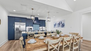Une cuisine moderne avec des meubles de couleur bleu foncé, des appareils en acier inoxydable et une table à manger en bois, accompagnée de huit chaises.