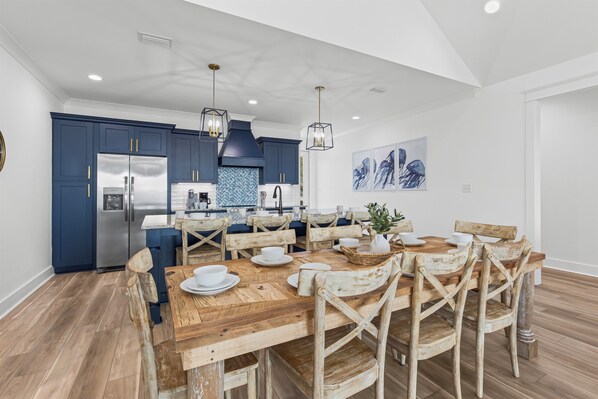 A modern kitchen with dark blue cabinets, stainless steel appliances, and a wooden dining table with eight chairs.