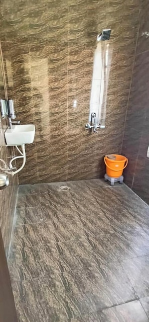A bathroom with a marble floor, a white sink, a shower with a glass door, and an orange bucket. - Hotel Imperial Inn Varanasi (Varanasi)