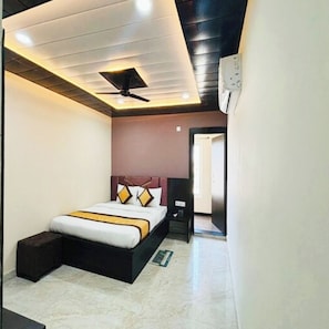 A bedroom with a bed, a ceiling fan, an air conditioning unit, and a door leading to another room. - Hotel Imperial Inn Varanasi (Varanasi)