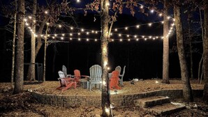 Un área de estar al aire libre con sillas Adirondack, un hogar de piedra y luces colgantes.