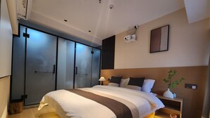 Habitació d'hotel moderna amb un llit gran, un armari, una taula de nit amb una làmpada i una petita planta.