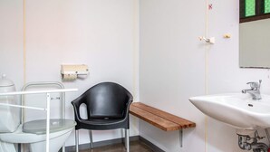 Un banyet petit amb un vàter blanc, una cadira negra, una prestatgeria de fusta i un lavabo.