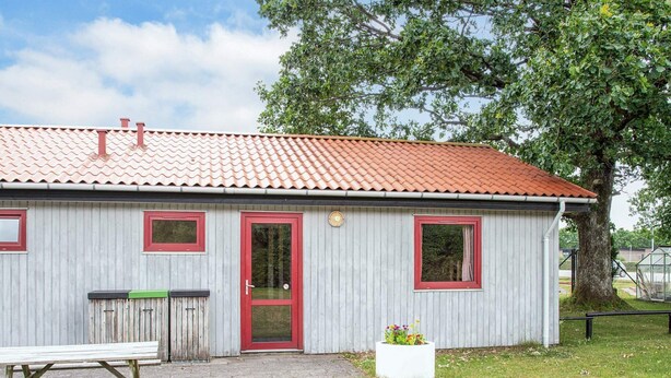 A small building with a red door and windows, a bench, and a planter with flowers. - 6 Person Holiday Park Home in Grindsted (Grindsted)