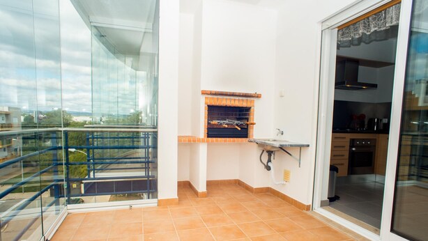 A balcony with a glass railing, a brick oven, and a sink. - Urbaniza o da Pegada Apartamento T2 (Tavira)