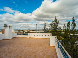 A rooftop terrace with a tiled floor, white walls, and a railing.