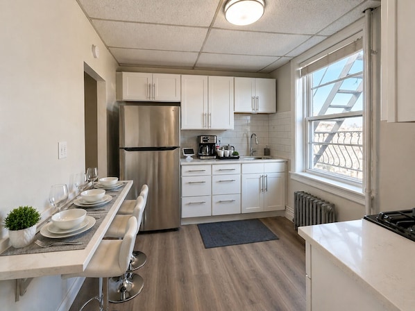 A modern kitchen with white cabinets, a stainless steel refrigerator, a coffee maker, and a window with a view.
