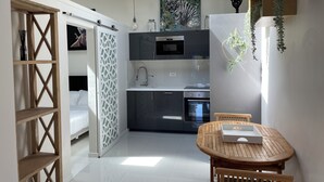 Una cocina moderna con microondas, horno y lavamanos, un área de comedor con mesa y sillas de madera, y un separador blanco con un diseño geométrico.