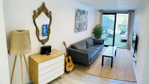 Una sala de estar moderna con un sofá gris, un mueble de madera, una guitarra, un cuadro y un ventanal con vistas al exterior.