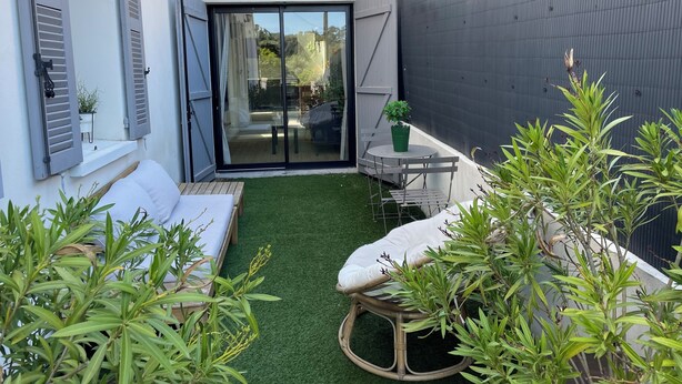 Un espacio exterior pequeño y cerrado con una zona de estar, una mesa y una planta en maceta.