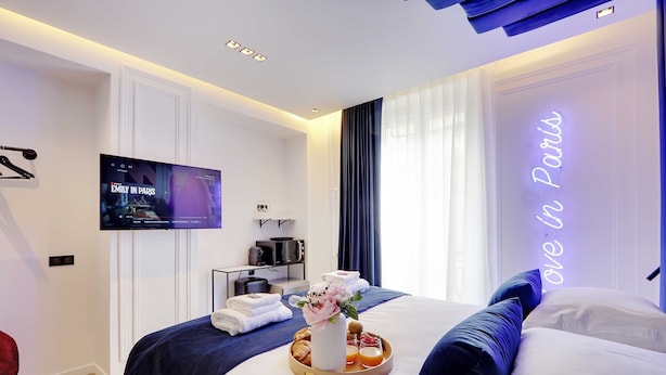 A modern hotel room with a bed, a TV, a tray with breakfast, and a neon sign. - Suberb Suite With Jacuzzi Le Marais Beaubourg (Paris)