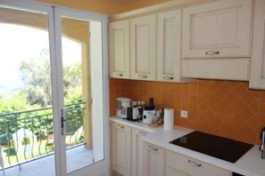 Cozinha com armários brancos, bancada preta e vista para o verde lá fora.