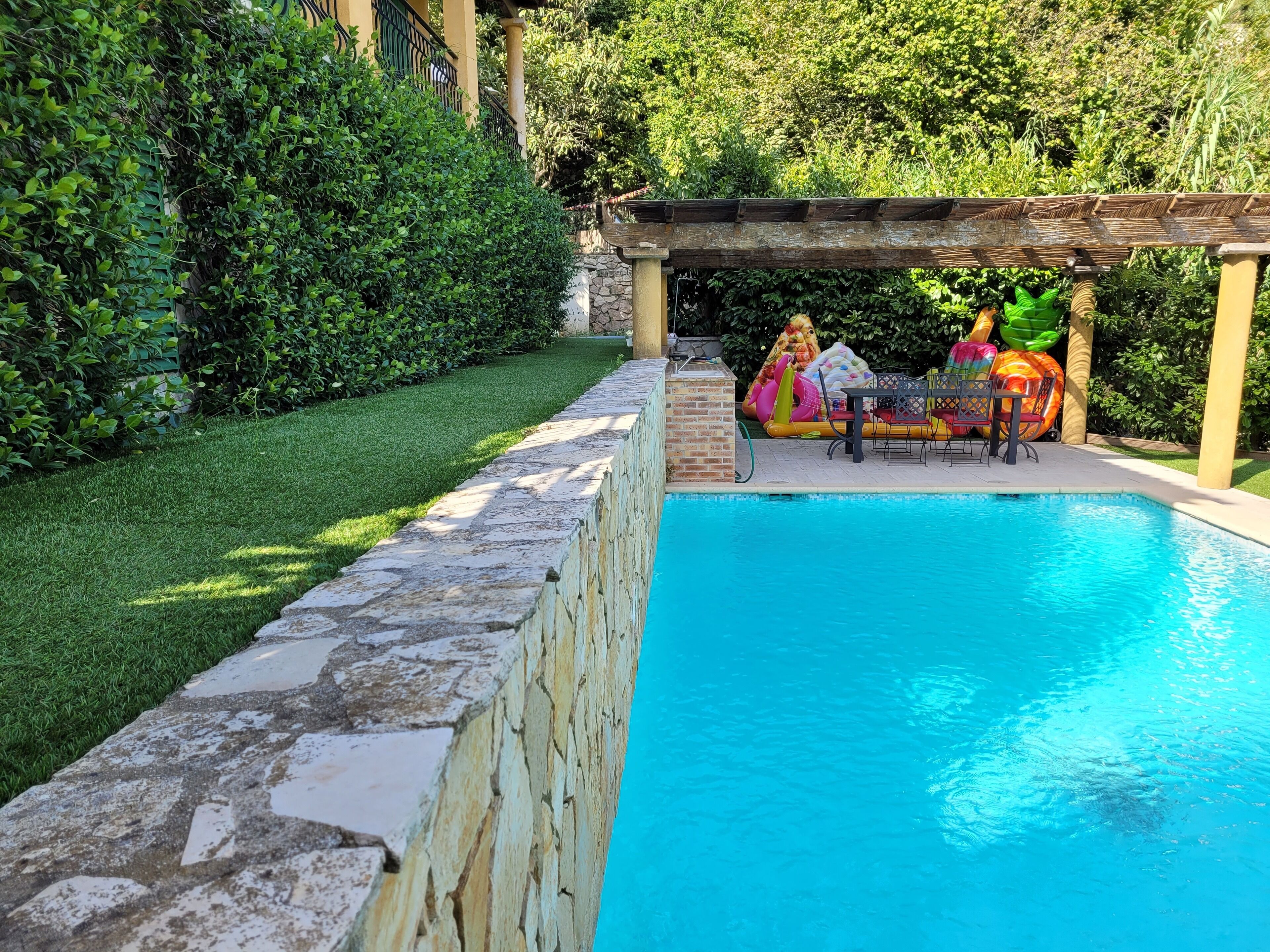Una piscina con un muro de piedra y una pérgola.