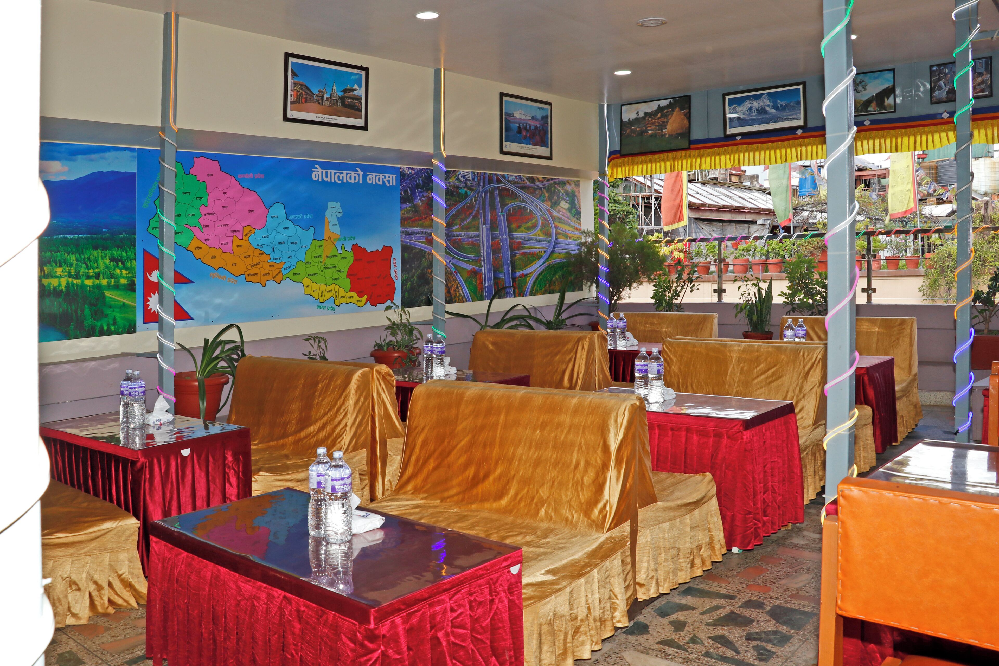 A restaurant with tables covered in red and gold tablecloths, a map on the wall, and framed pictures on the ceiling.