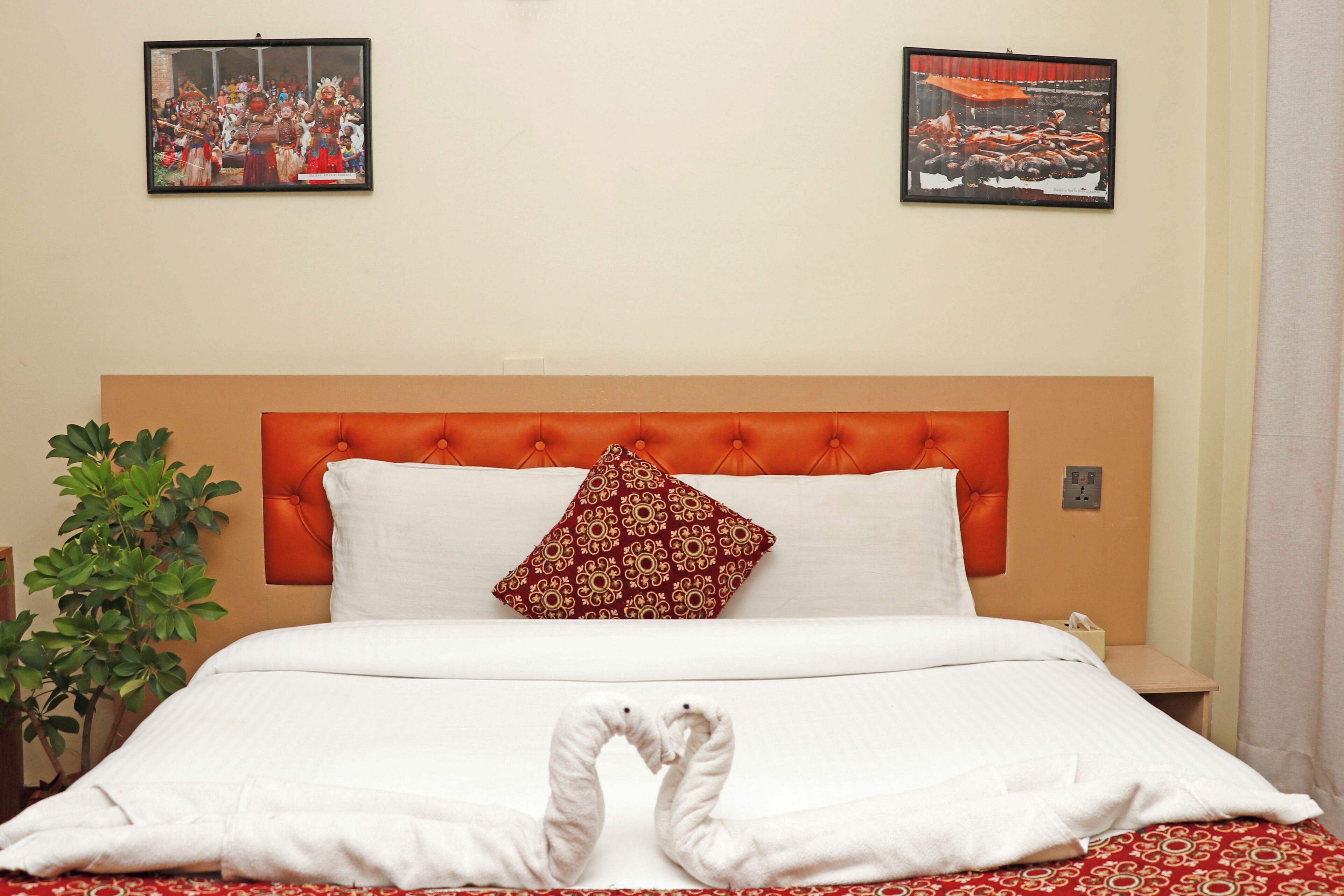 A hotel room with a large bed, a red headboard, a red patterned pillow, and two framed pictures on the wall.