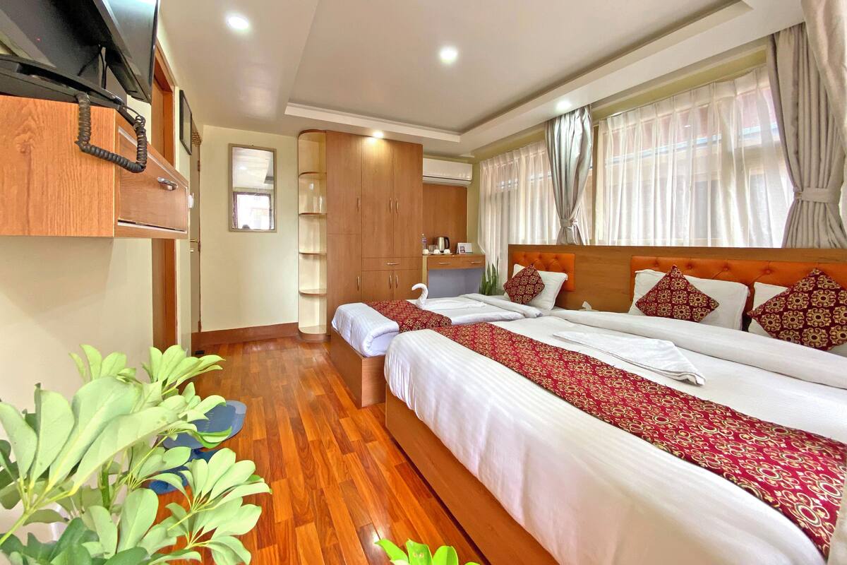 Habitació d'hotel amb dos llits, sòl de fusta, televisió penjada a la paret i finestra amb cortines.