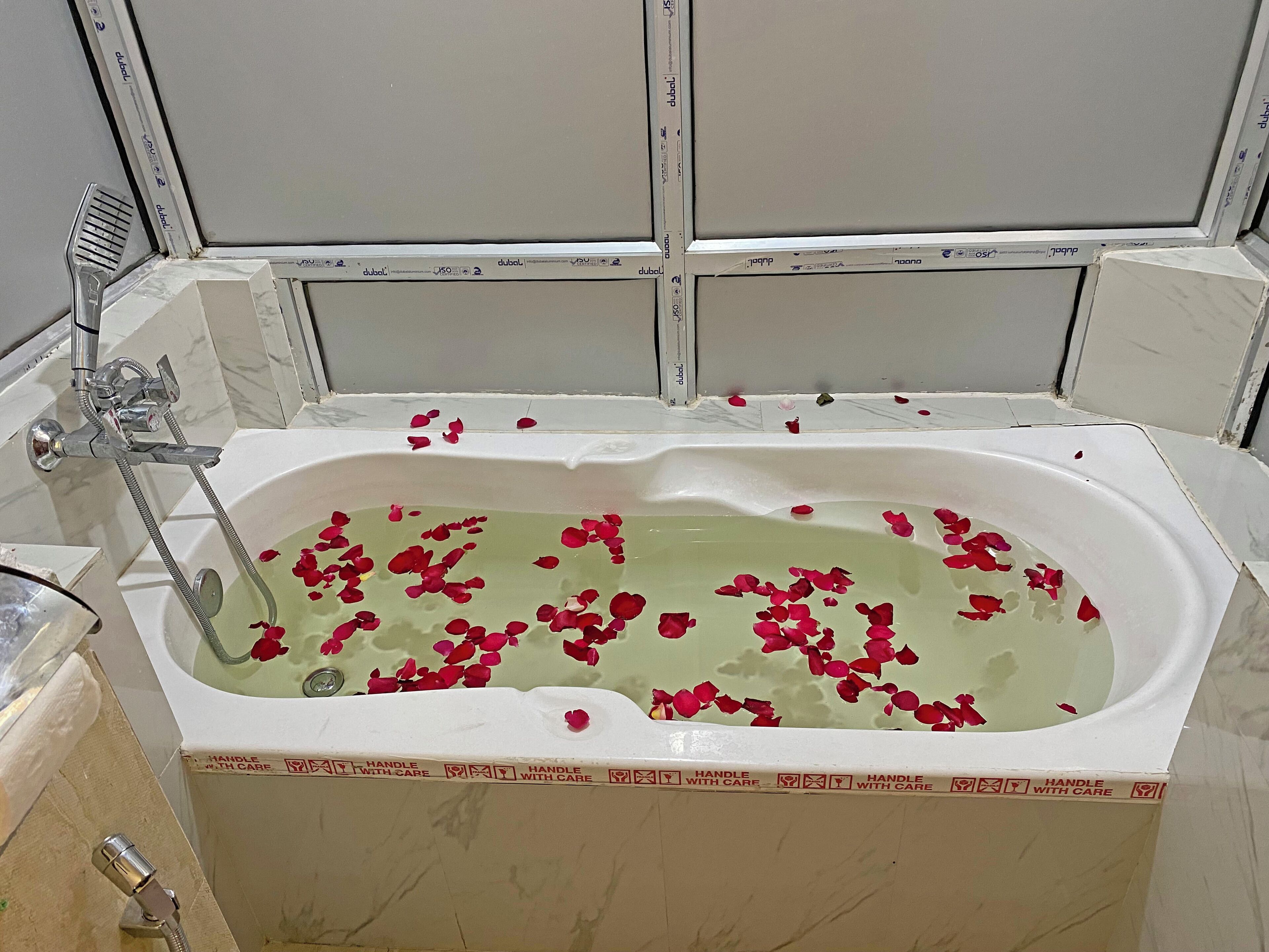 Une baignoire dans laquelle flottent des pétales de rose, une pomme de douche et une poignée avec des instructions d’entretien.