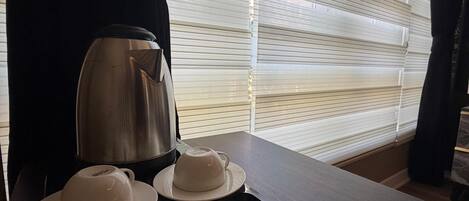 A hotel room with a dining table set with a teapot, two cups, and a tray with tea bags and a packet of Doritos.