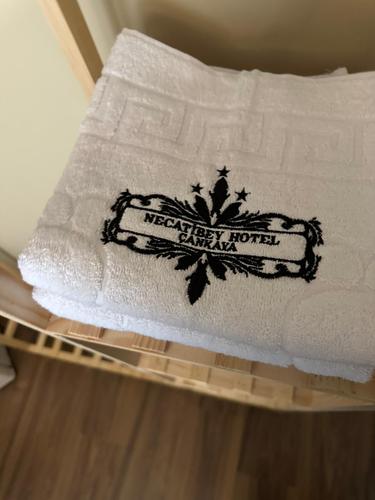 A white towel with a black embroidered logo that reads "NECATBEY HOTEL CANKAYA".