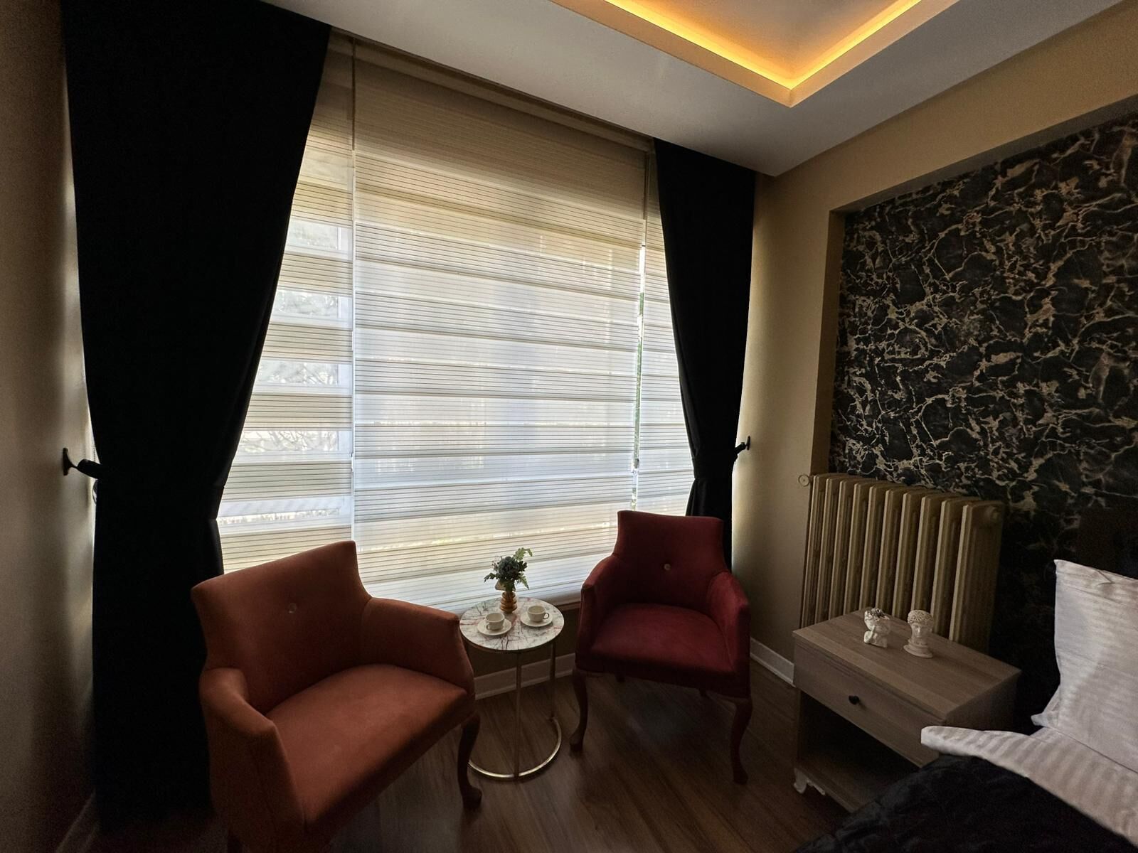 Habitación de hotel con cama, dos sillones, una mesita redonda con una planta y un adorno en la pared.