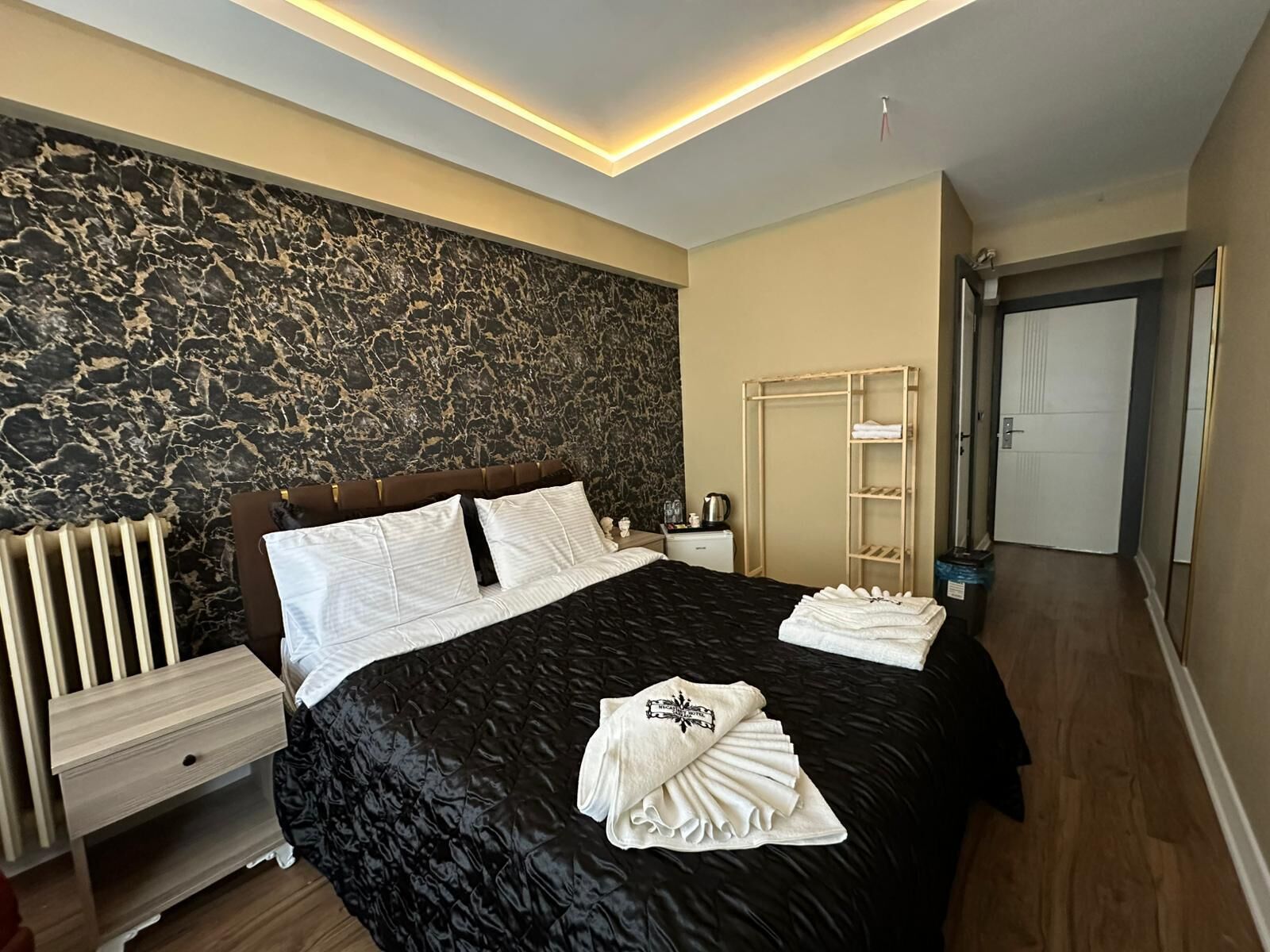 A modern bedroom with a marble wall, a black bedspread, a wooden nightstand, a bedside table, and a wardrobe.