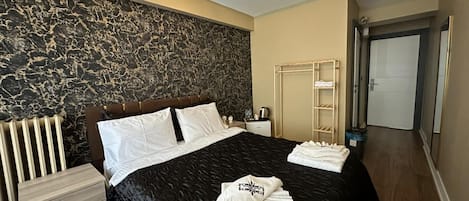 A modern bedroom with a marble wall, a black bedspread, a wooden nightstand, a bedside table, and a wardrobe.