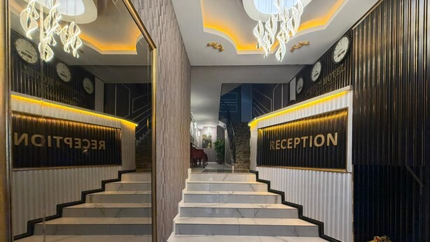 Un área de recepción con una escalera que conduce al piso superior, con un diseño moderno, escalones de mármol y señalización de recepción iluminada.