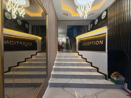 Un área de recepción con una escalera que conduce al piso superior, con un diseño moderno, escalones de mármol y señalización de recepción iluminada.