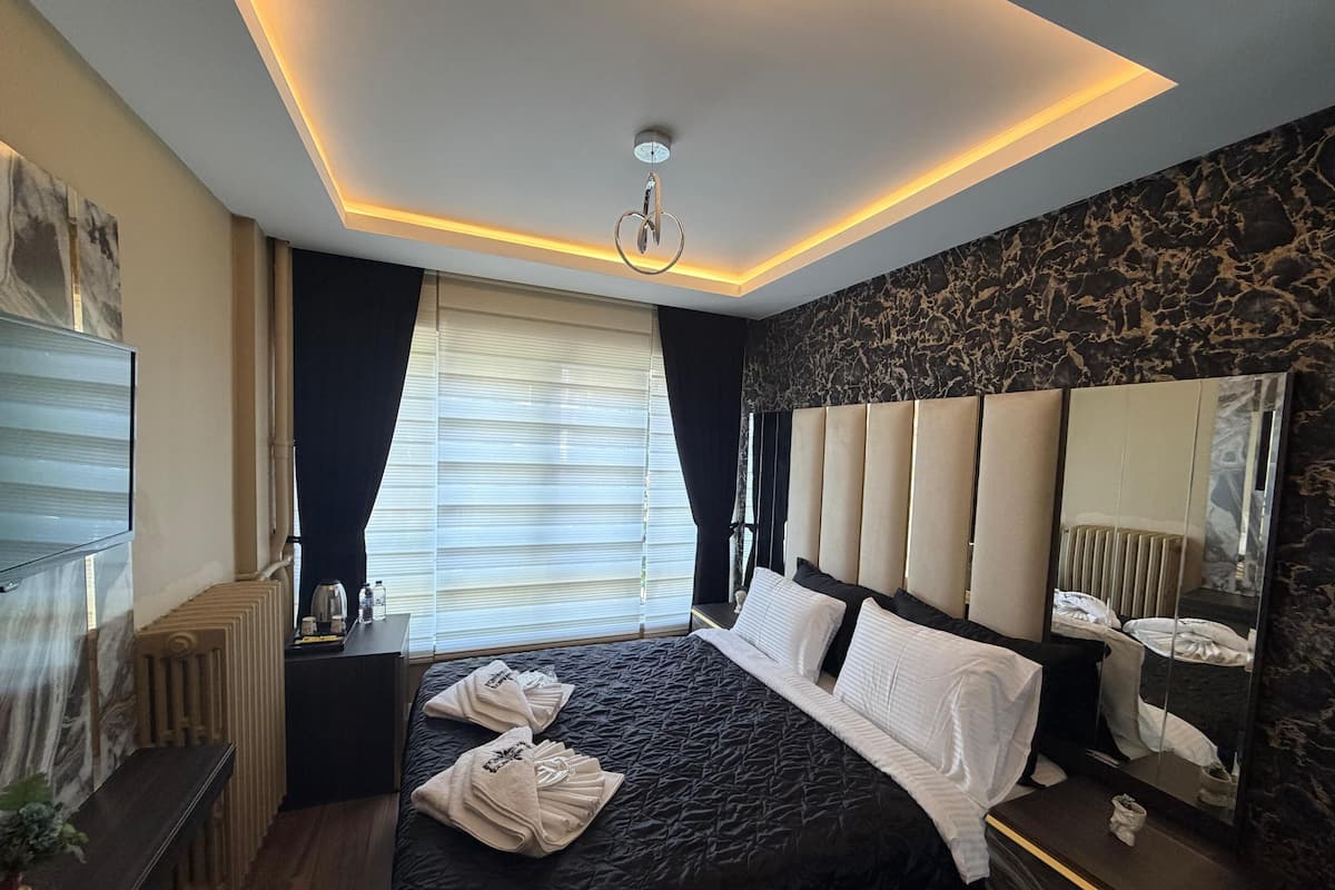 A modern hotel room with a large bed, a bedside table, a mirror, and a window with blinds.