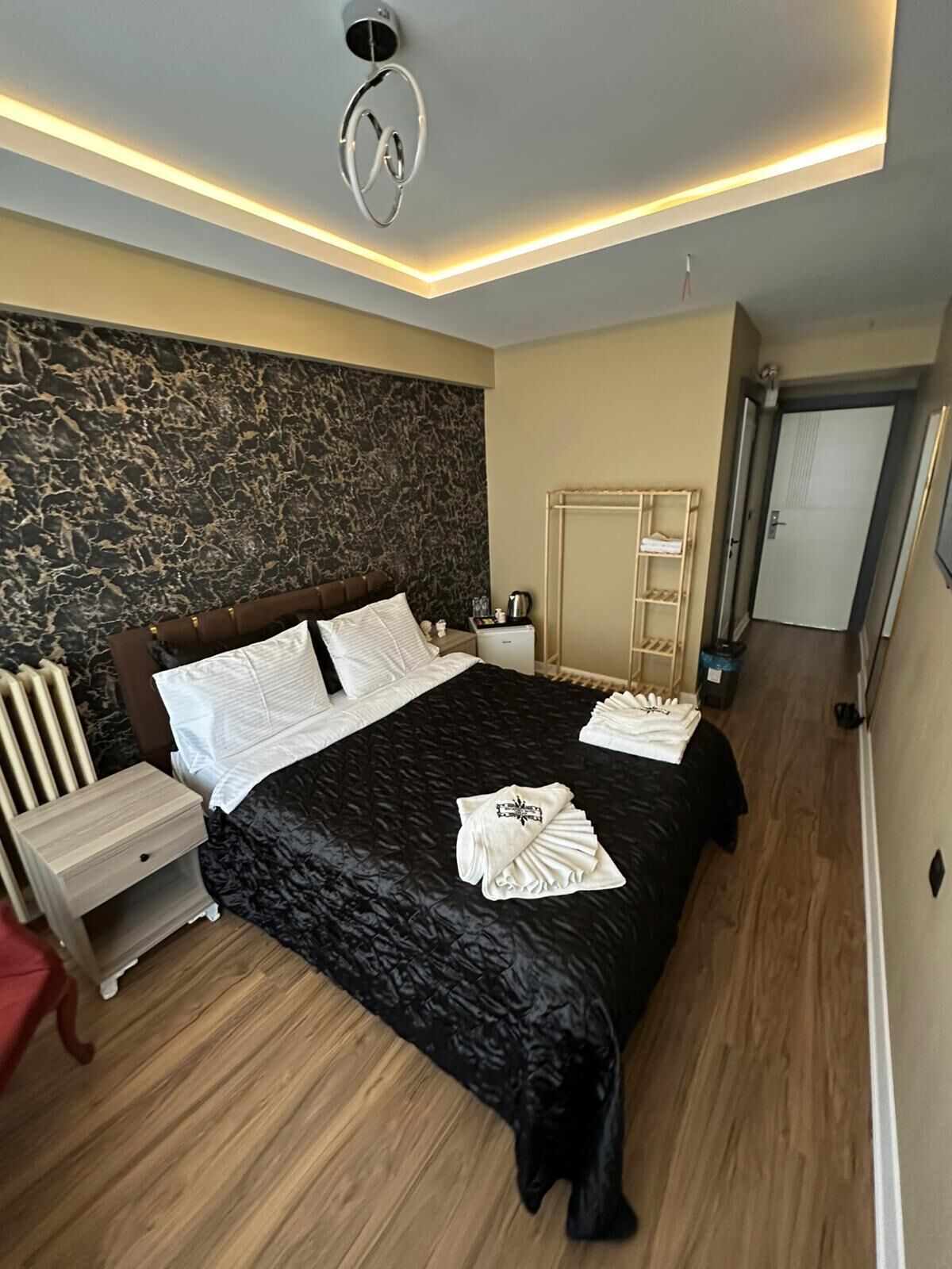 A modern bedroom with a large bed, a headboard with a unique design, a bedside table, a nightstand, a radiator, and a wardrobe.