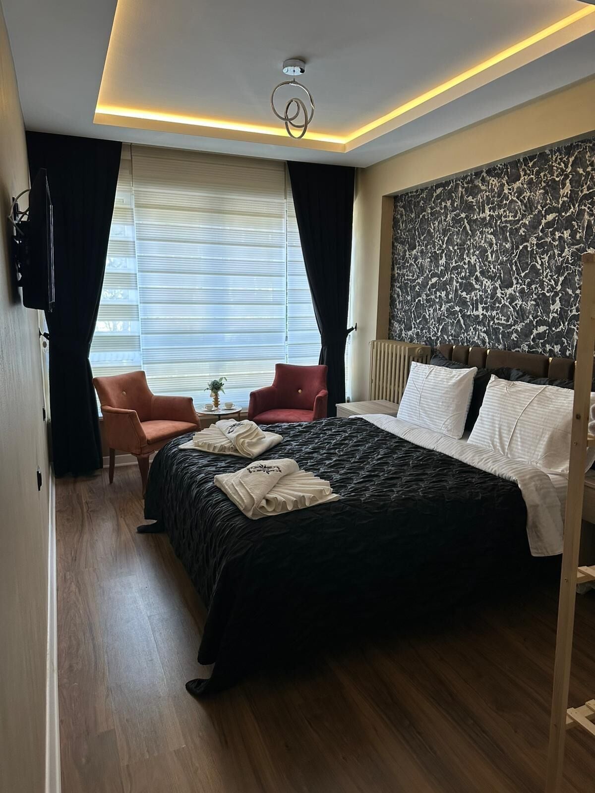 A hotel room with a large bed, a desk with a chair, a TV, and a window with curtains.