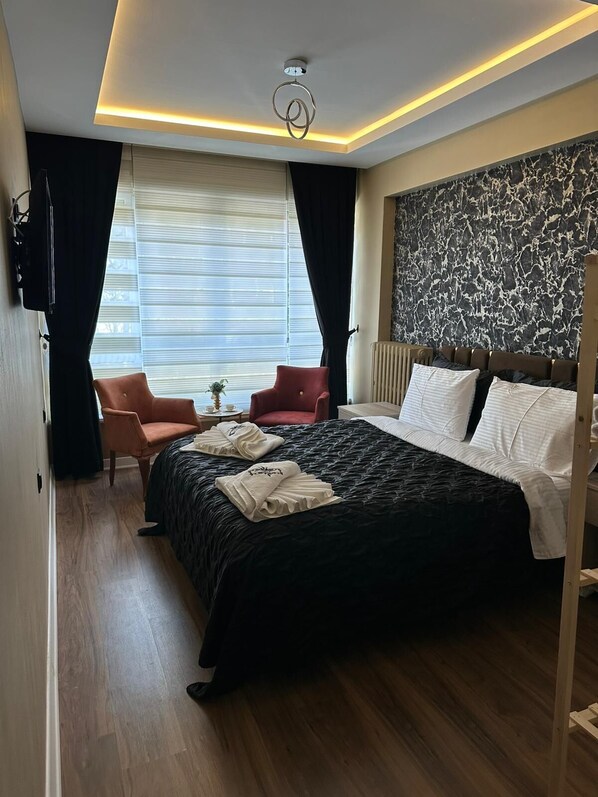 Una habitación de hotel con una cama grande, un escritorio con silla, un televisor y una ventana con cortinas.