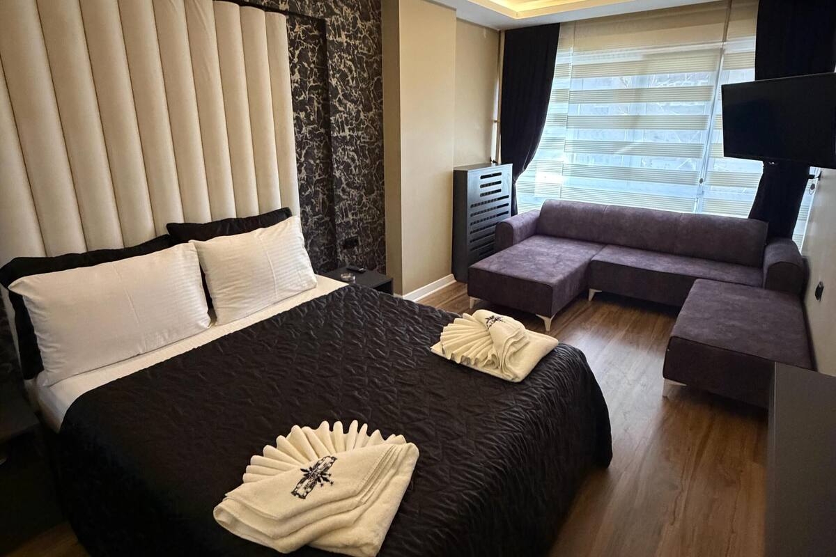 A modern hotel room with a large bed, a sofa, a TV, and a ceiling light.